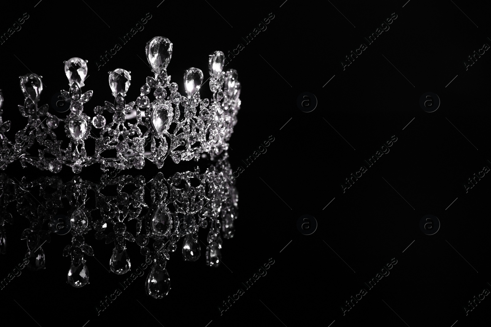 Photo of Beautiful silver tiara with diamonds on dark mirror surface. Space for text