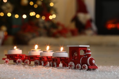 Toy train with burning candles near Christmas tree in room, closeup. Space for text