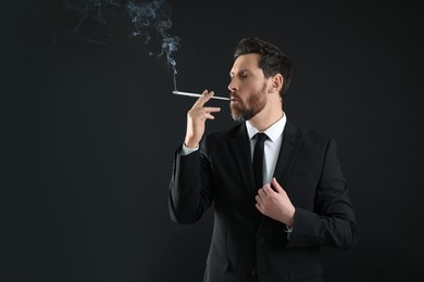 Man using long cigarette holder for smoking on black background, space for text