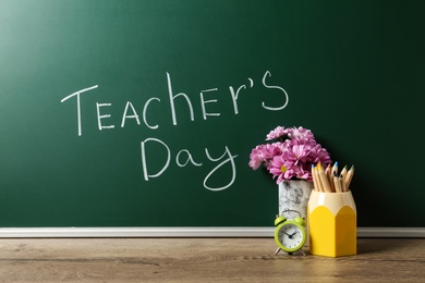 Green chalkboard with inscription TEACHER'S DAY and vase of flowers on wooden table