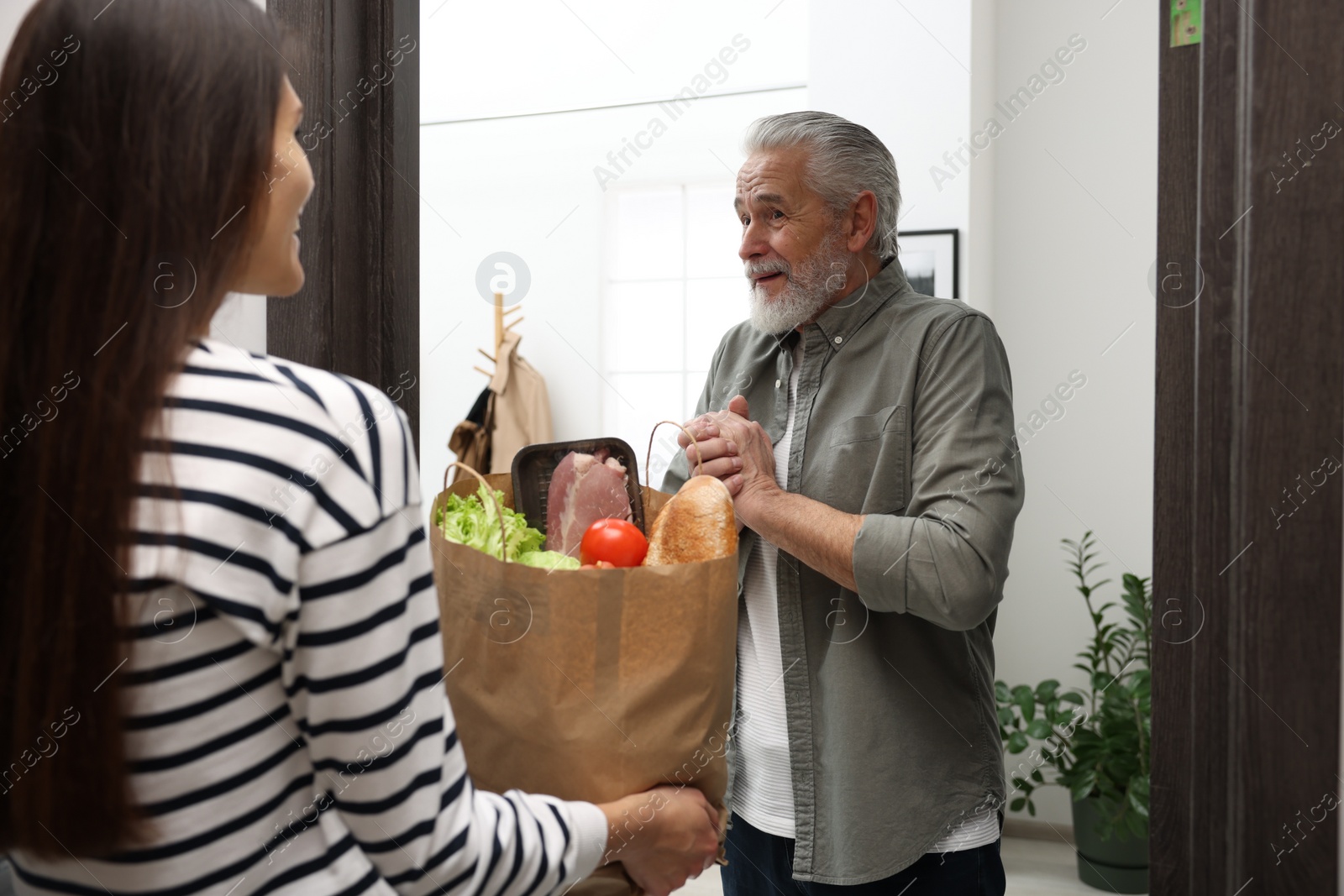 Photo of Courier giving paper bag with food products to senior man indoors