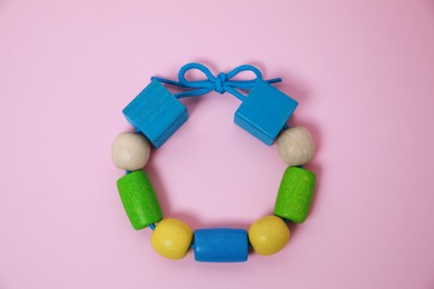 Wooden pieces and string for threading activity on pink background, top view. Educational toy for motor skills development