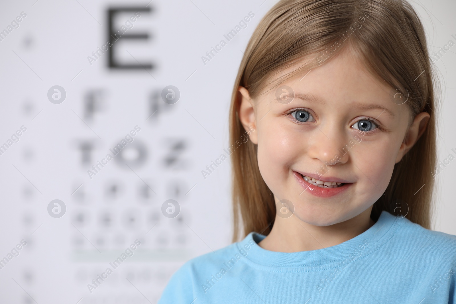 Photo of Cute little girl against vision test chart