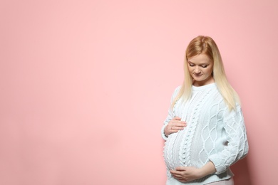 Beautiful pregnant woman in sweater on color background. Space for text