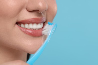 Photo of Woman brushing her teeth with plastic toothbrush on light blue background, closeup. Space for text