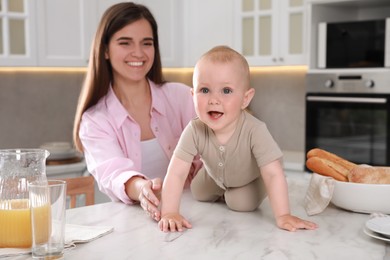 Photo of Happy young woman and her cute little baby spending time together in kitchen