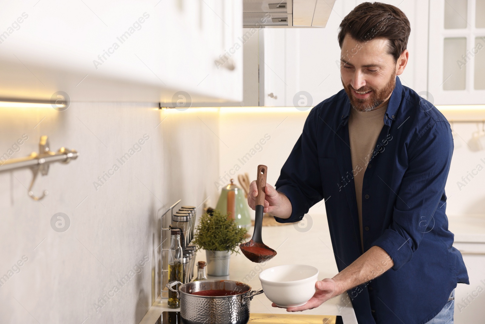 Photo of Man pouring delicious tomato soup into bowl in kitchen