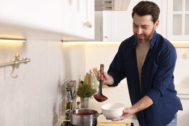 Man pouring delicious tomato soup into bowl in kitchen