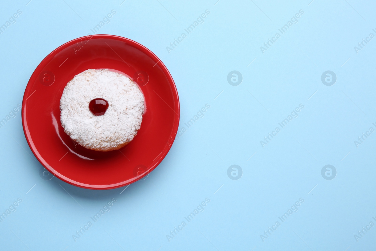 Photo of Hanukkah donut with jelly and powdered sugar on light blue background, top view. Space for text