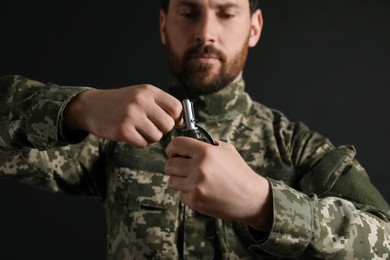 Photo of Soldier pulling safety pin out of hand grenade on black background, selective focus. Military service