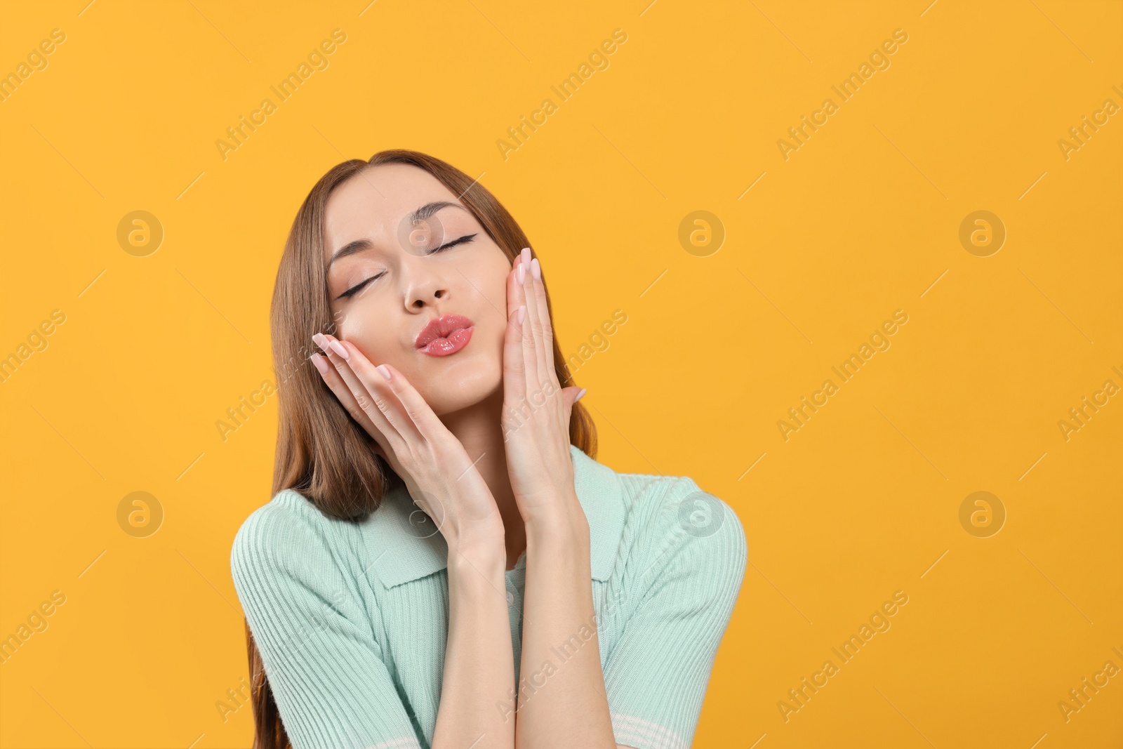 Photo of Beautiful young woman blowing kiss on yellow background, space for text