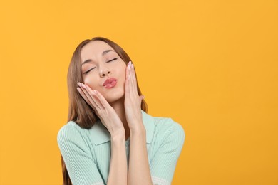 Beautiful young woman blowing kiss on yellow background, space for text