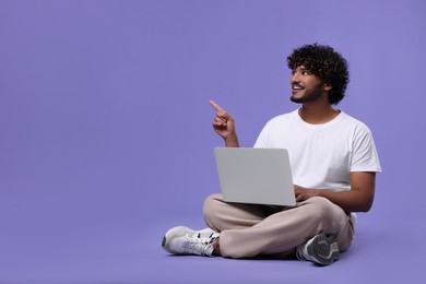 Photo of Happy man with laptop on purple background, space for text