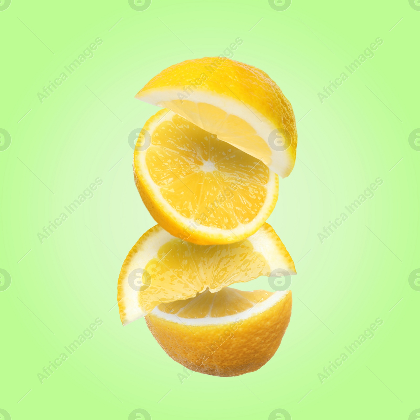 Image of Cut fresh lemons falling on light green background