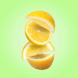Image of Cut fresh lemons falling on light green background