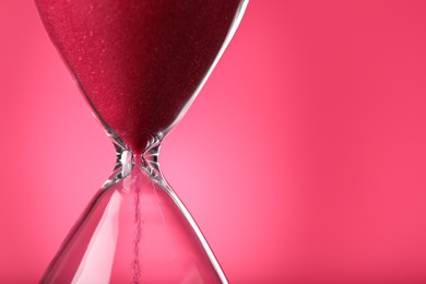 Hourglass with flowing sand on pink background, closeup. Space for text