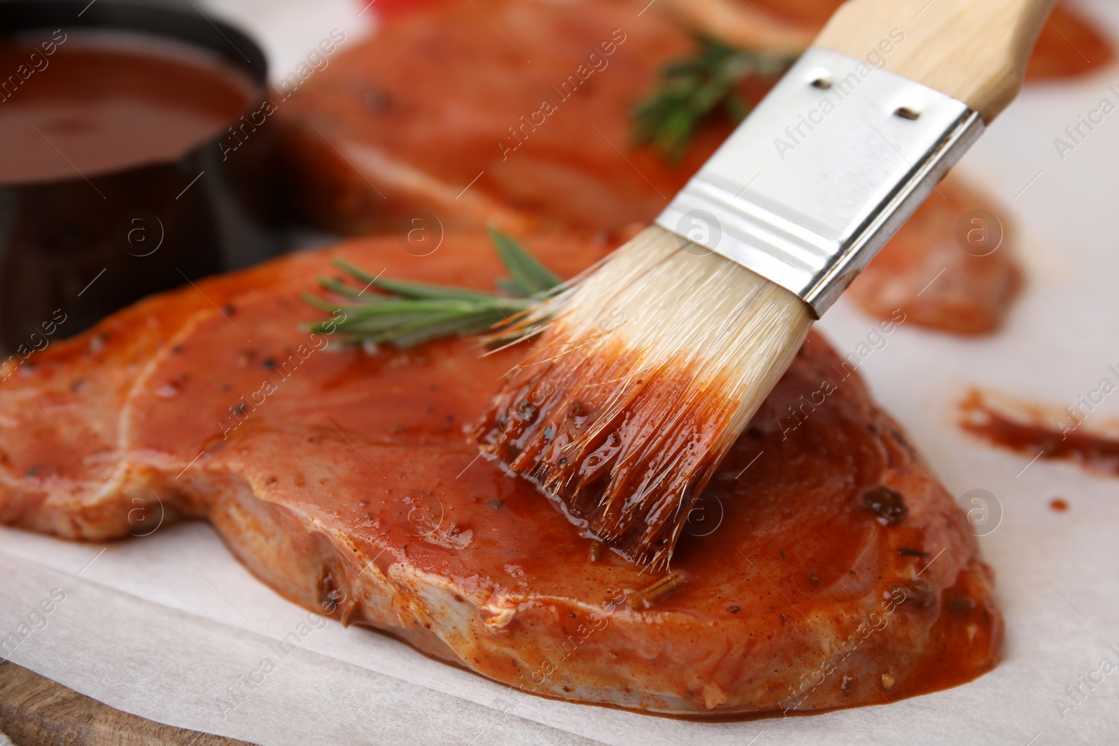 Photo of Spreading marinade onto raw meat with basting brush on table, closeup