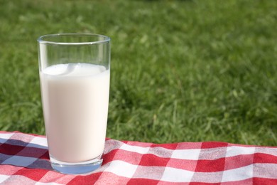 Photo of Glass of fresh milk on checkered blanket outdoors. Space for text