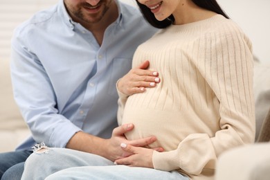 Photo of Pregnant woman with her husband touching belly on sofa at home, closeup