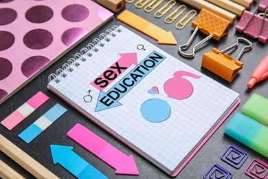 Image of Notebook with text Sex Education, heart, female and male gender signs, woman and man drawings among other stationery on table