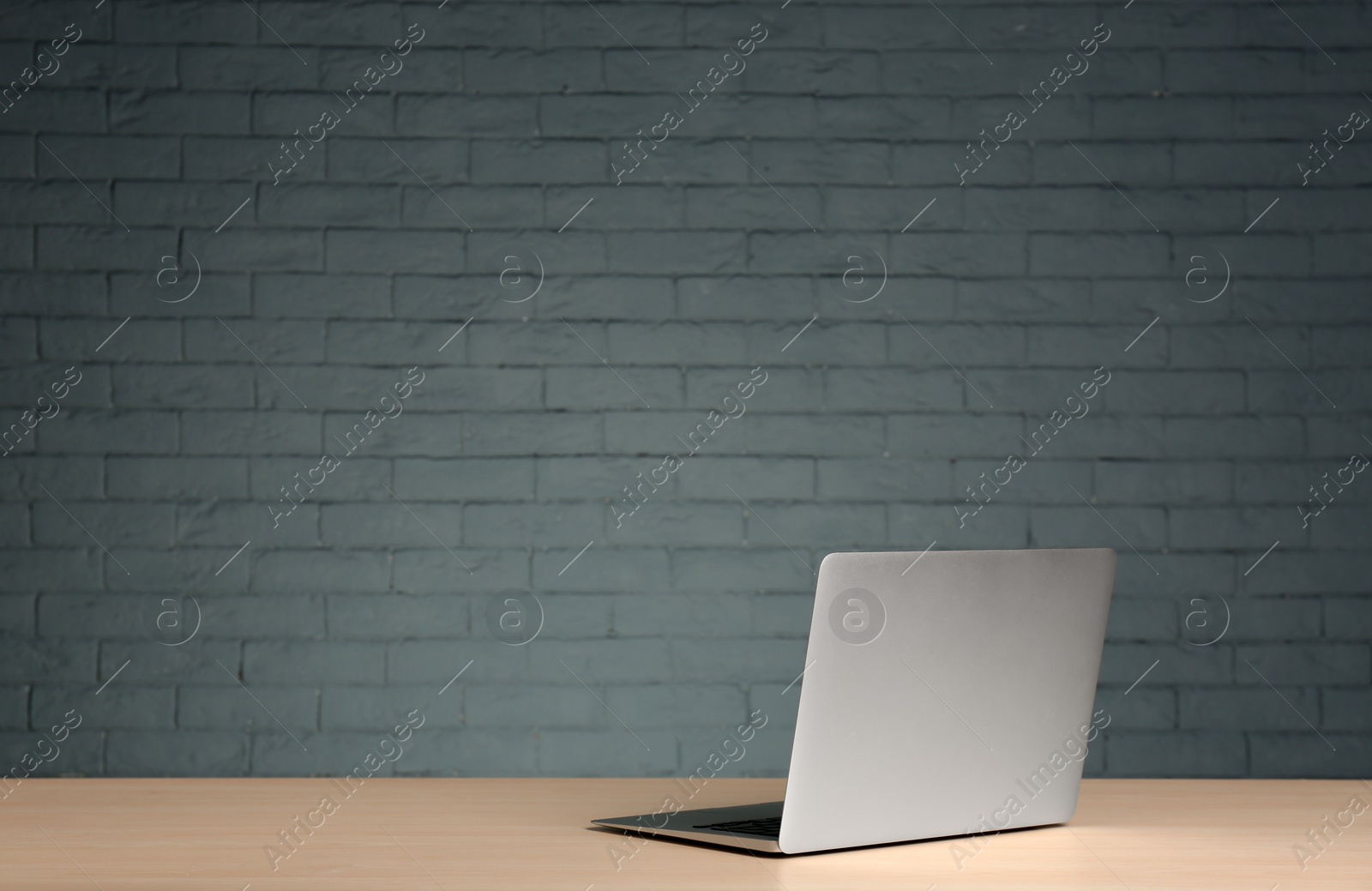 Photo of Modern laptop on table against brick wall