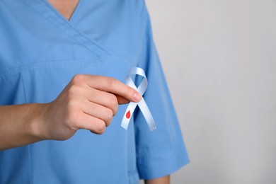 Photo of Doctor holding light blue ribbon with paper blood drop on grey background, closeup. World Diabetes Day