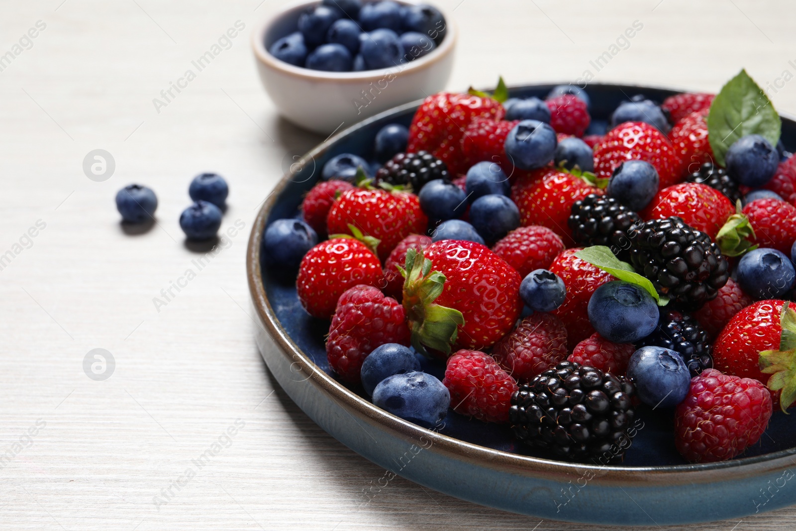 Photo of Different fresh ripe berries on light wooden table, closeup. Space for text