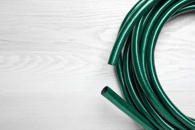 Green garden hose on white wooden table, top view. Space for text