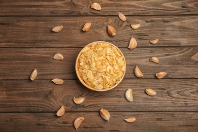 Cloves and bowl with dried garlic flakes on wooden background, top view