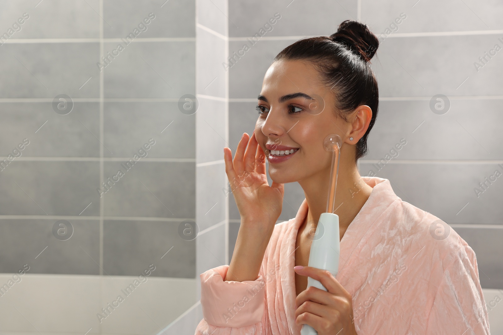 Photo of Woman using high frequency darsonval device in bathroom, space for text