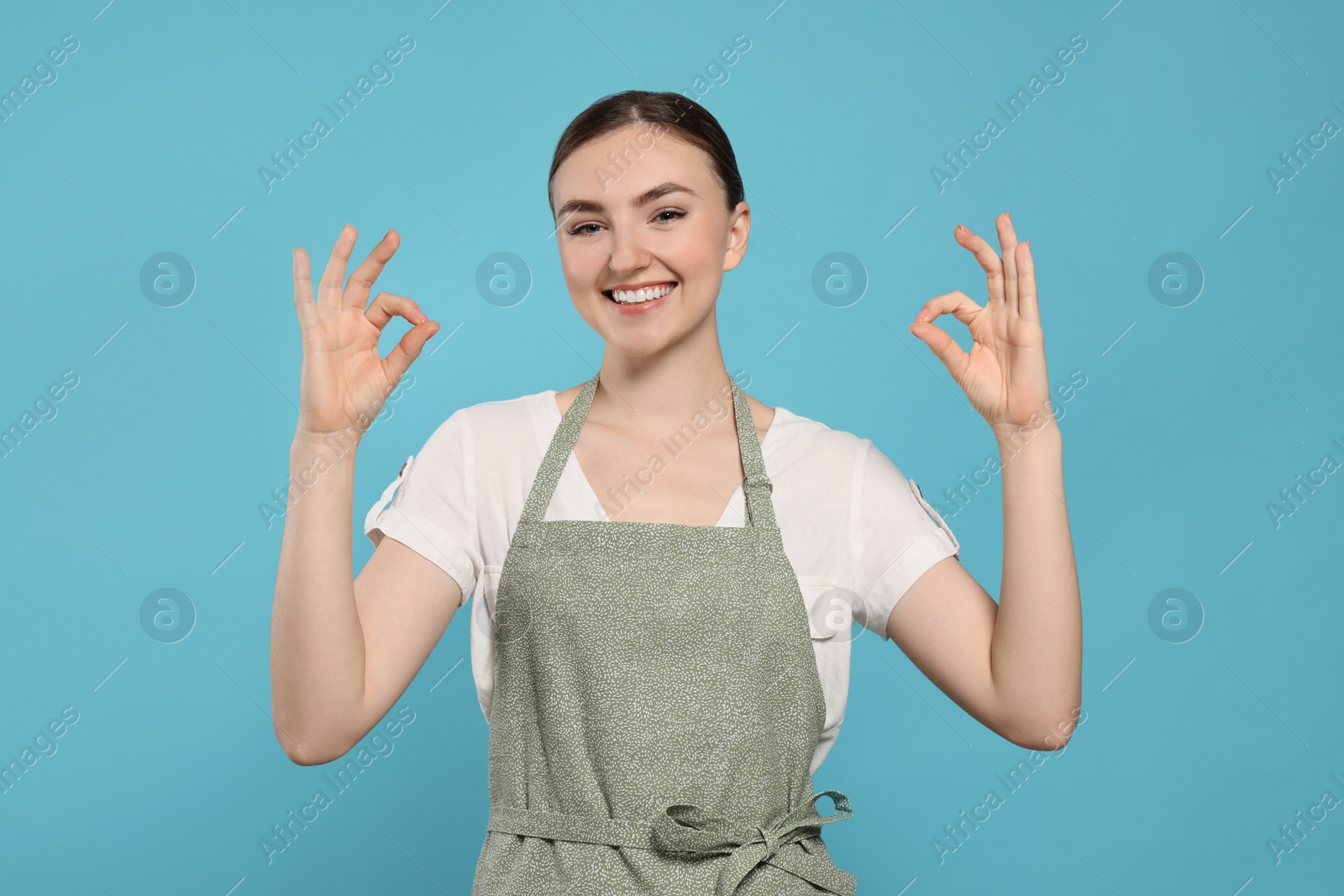 Photo of Beautiful young woman in clean apron with pattern on light blue background