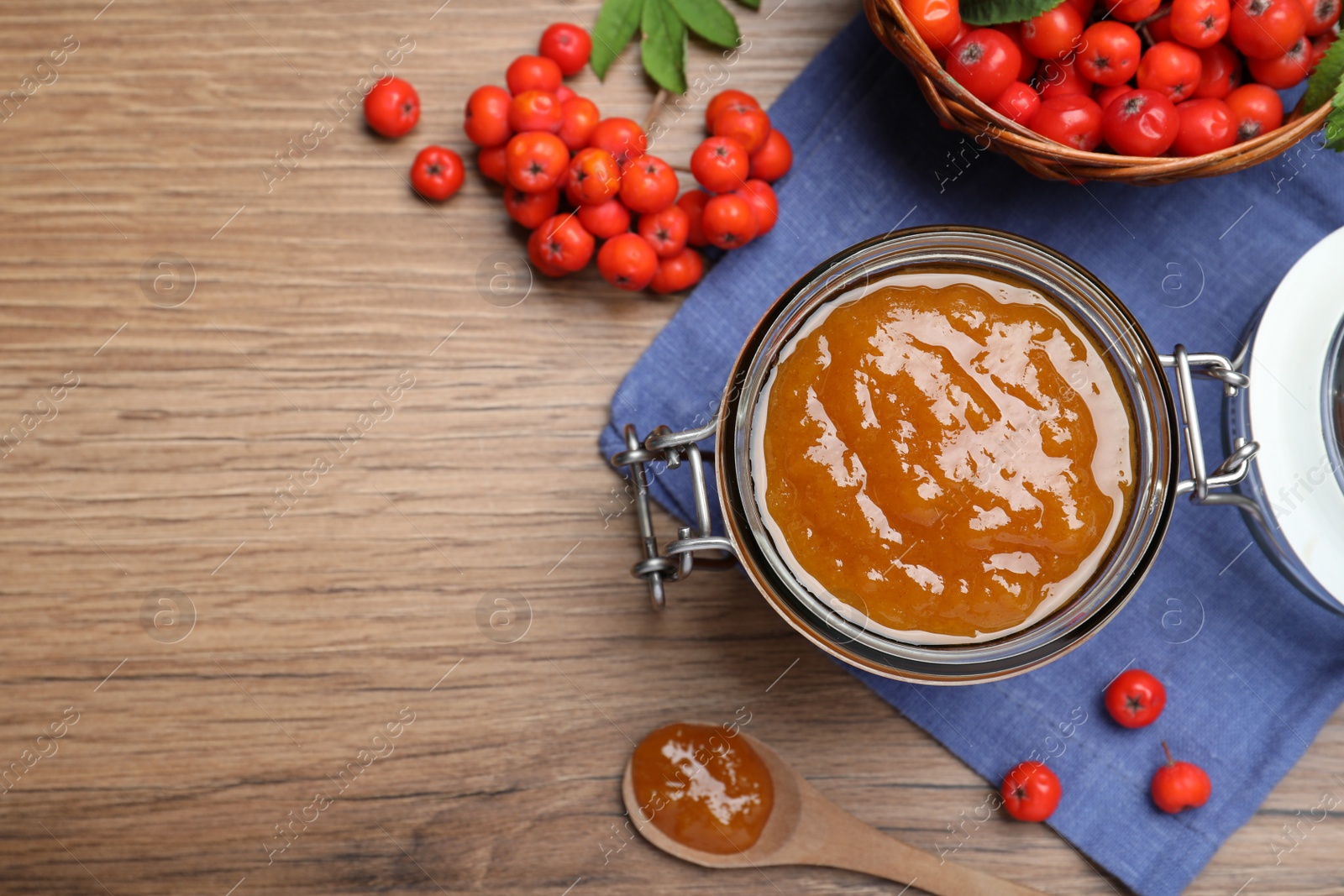 Photo of Flat lay composition with delicious rowan jam and berries on wooden table. Space for text