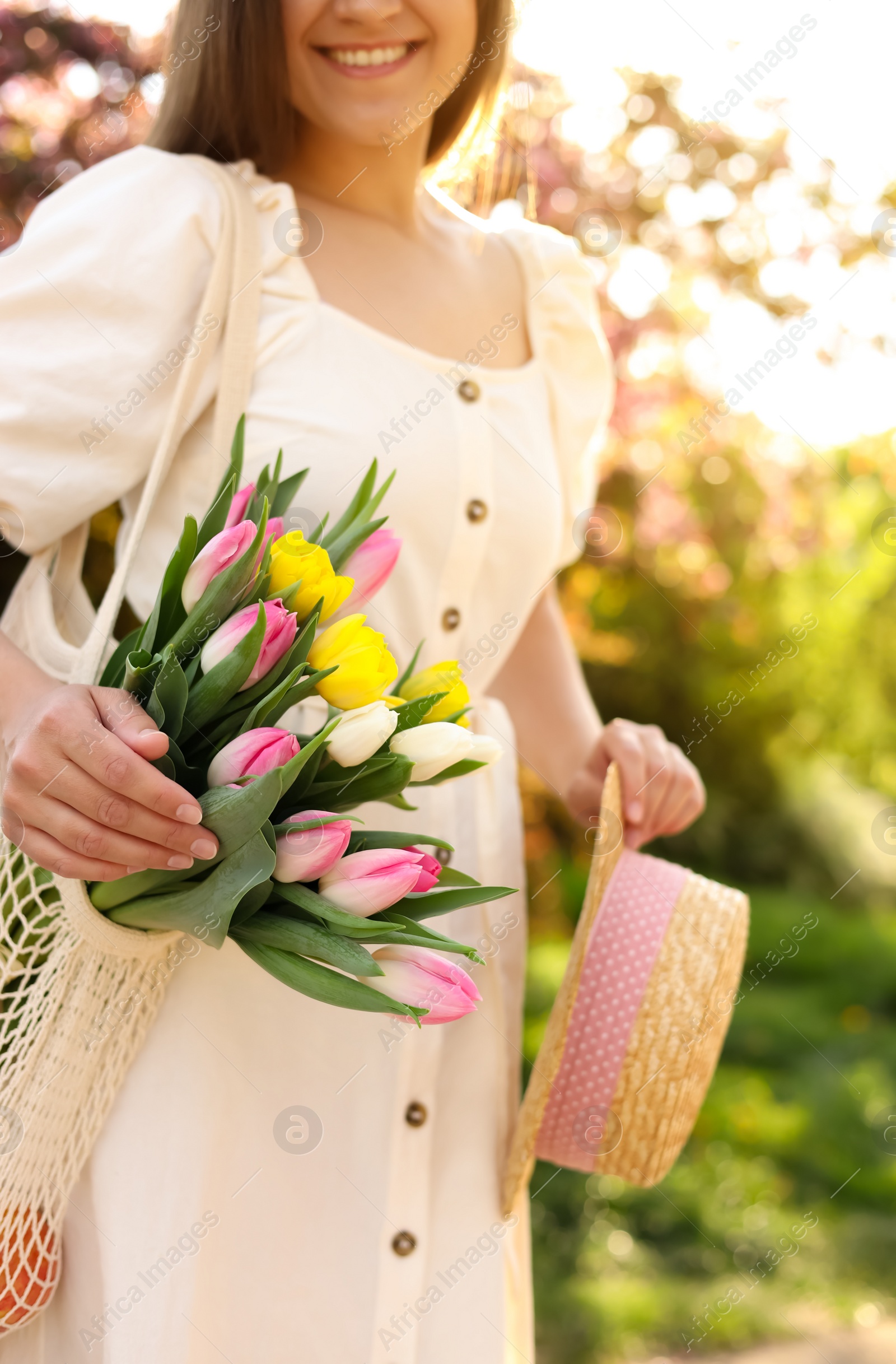 Photo of Young woman with bouquet of tulips and hat in park on sunny day, closeup