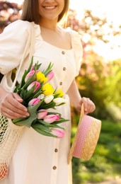 Photo of Young woman with bouquet of tulips and hat in park on sunny day, closeup