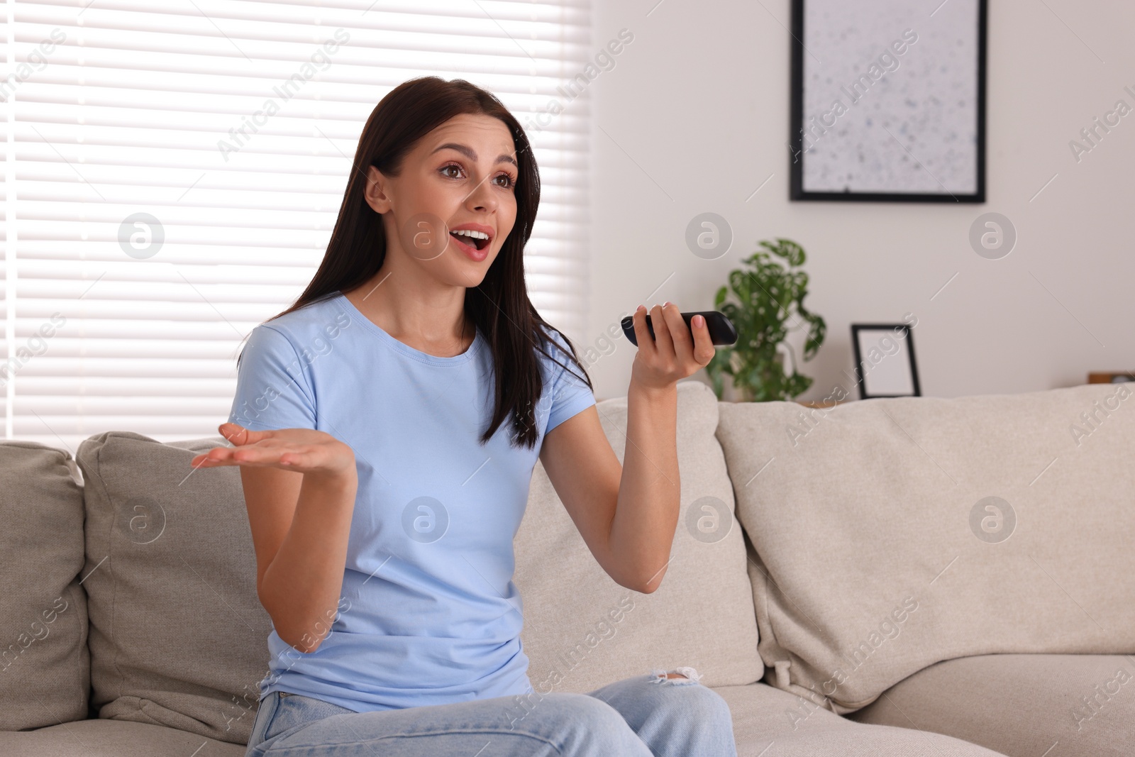 Photo of Emotional woman with remote controller watching TV on sofa at home