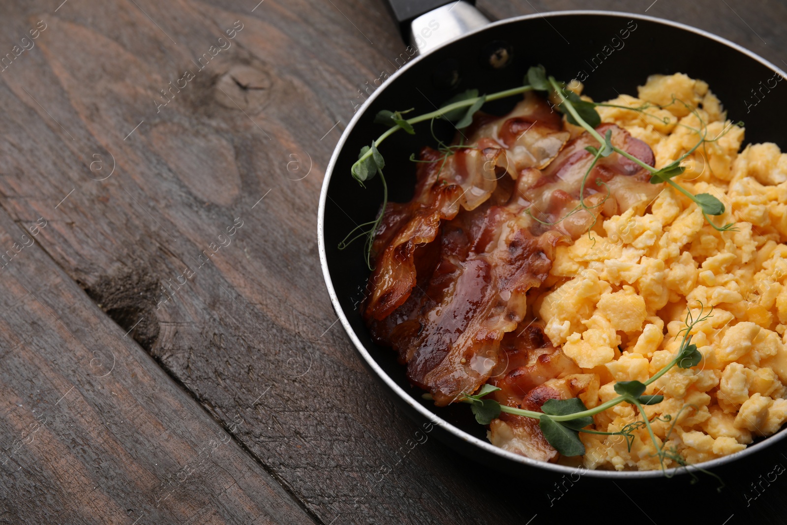 Photo of Delicious scrambled eggs with bacon in frying pan on wooden table. Space for text