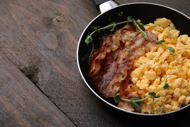 Photo of Delicious scrambled eggs with bacon in frying pan on wooden table. Space for text