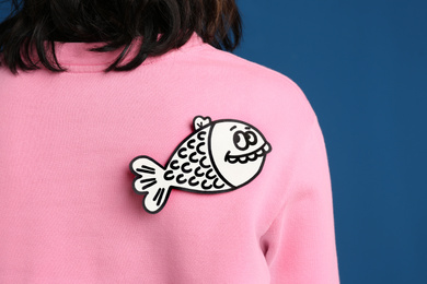 Woman with paper fish on back against blue background, closeup. April fool's day