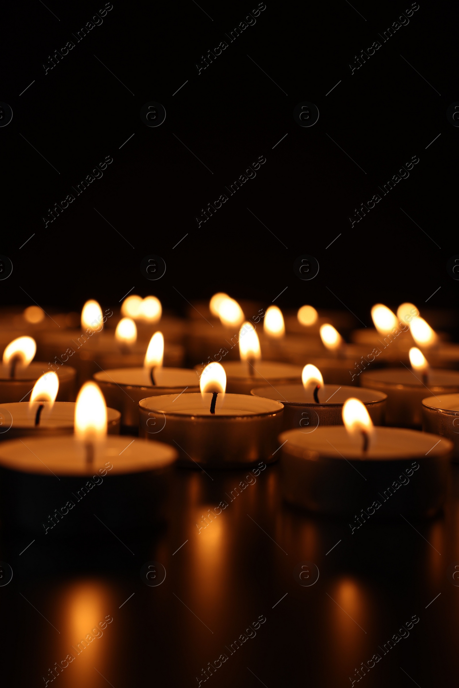 Photo of Burning candles on dark surface against black background