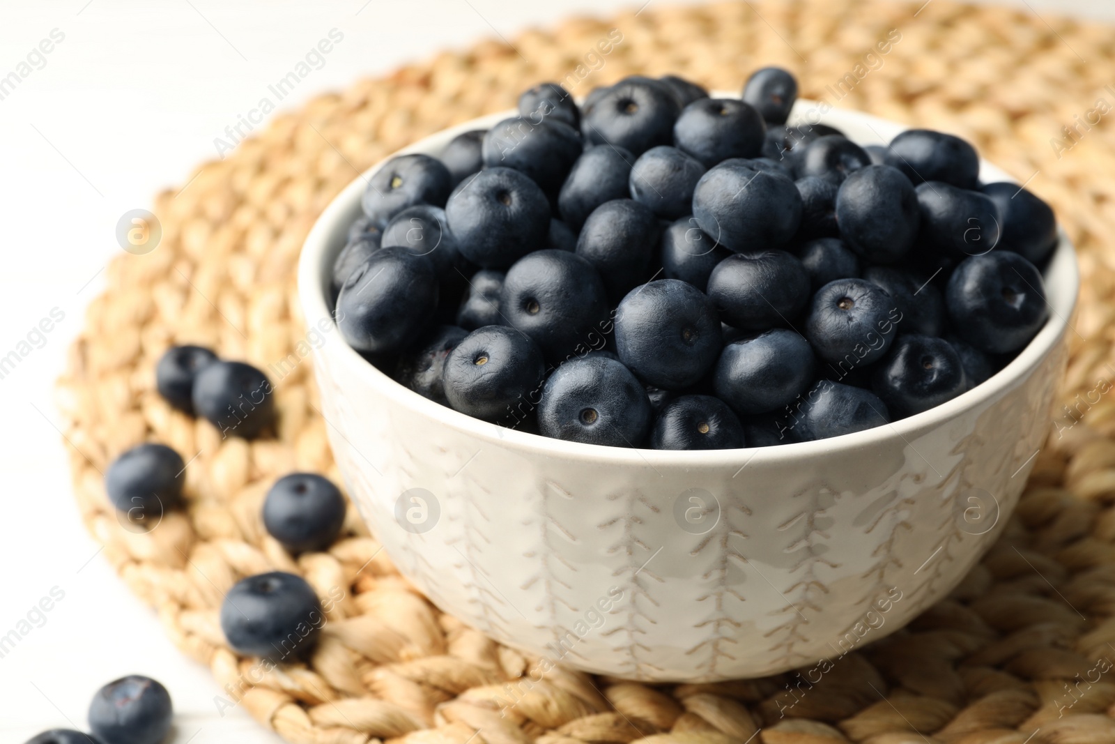 Photo of Bowl of fresh acai berries on wicker mat, closeup view. Space for text