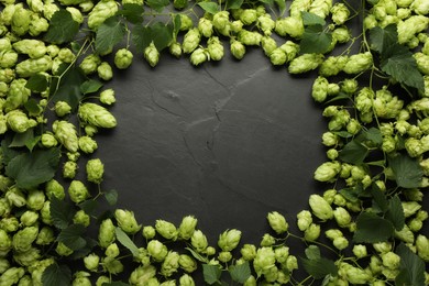 Frame of fresh green hops and leaves on black table, flat lay. Space for text