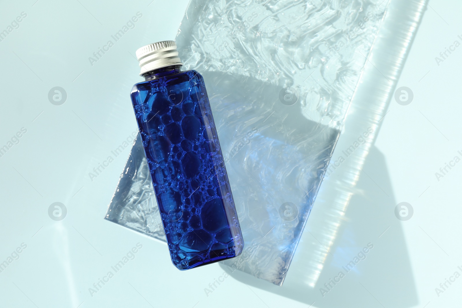 Photo of Bottle of cosmetic product on light blue background, top view