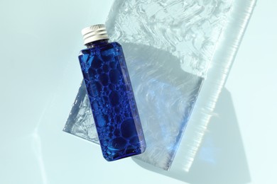 Bottle of cosmetic product on light blue background, top view