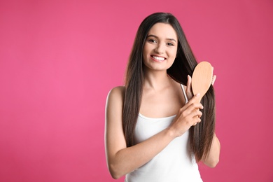 Beautiful smiling young woman with hair brush on color background