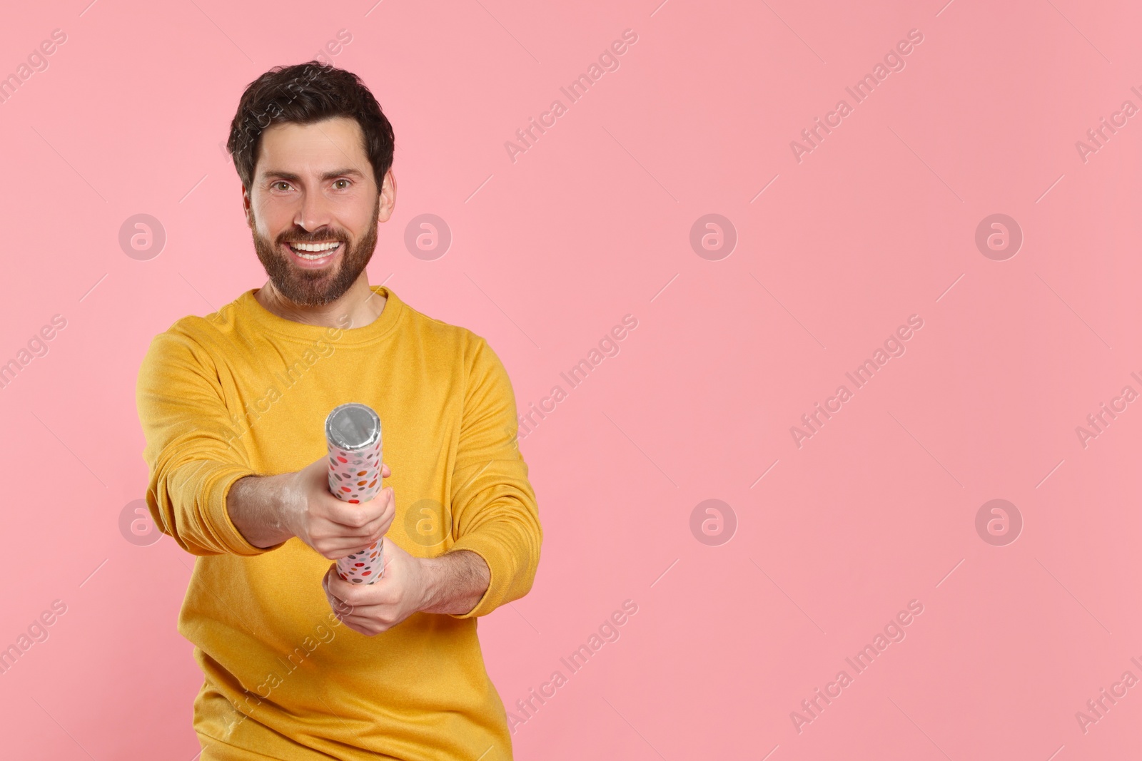 Photo of Happy man with party popper on pink background. Space for text