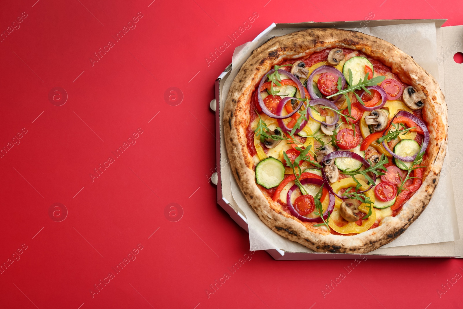 Photo of Delicious vegetable pizza in cardboard box on red background, top view. Space for text