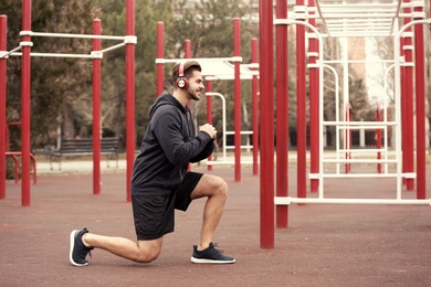 Photo of Young man with headphones listening to music and exercising on sports ground