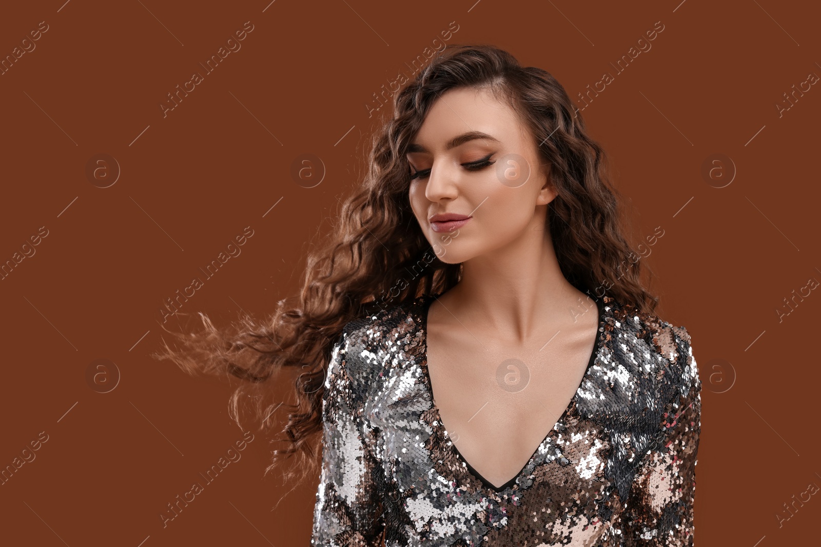 Photo of Beautiful young woman with long curly hair in sequin dress on brown background, space for text