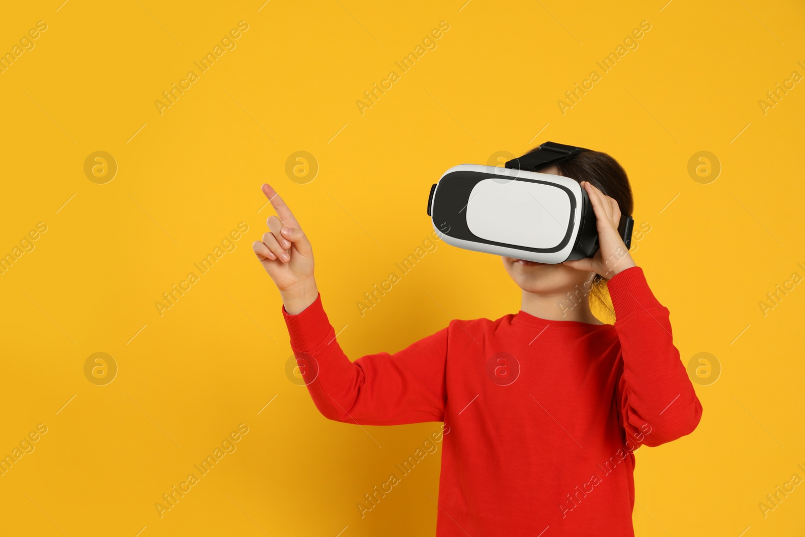 Photo of Little girl using virtual reality headset on yellow background