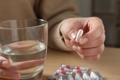 Photo of Woman with glass of water and pill at wooden table, closeup